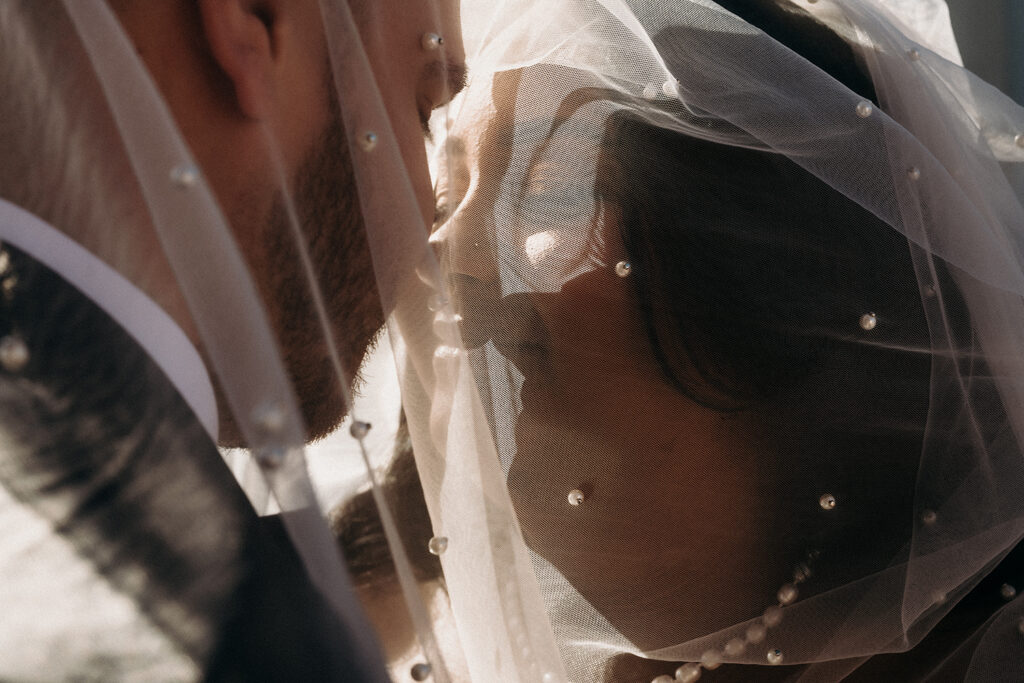 Photo of a bride and groom under the veil with sun shining through on a rooftop in Brooklyn, NY