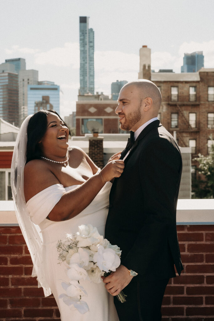 Bride and groom laughing together during wedding photos on a rooftop in Brooklyn, NY.