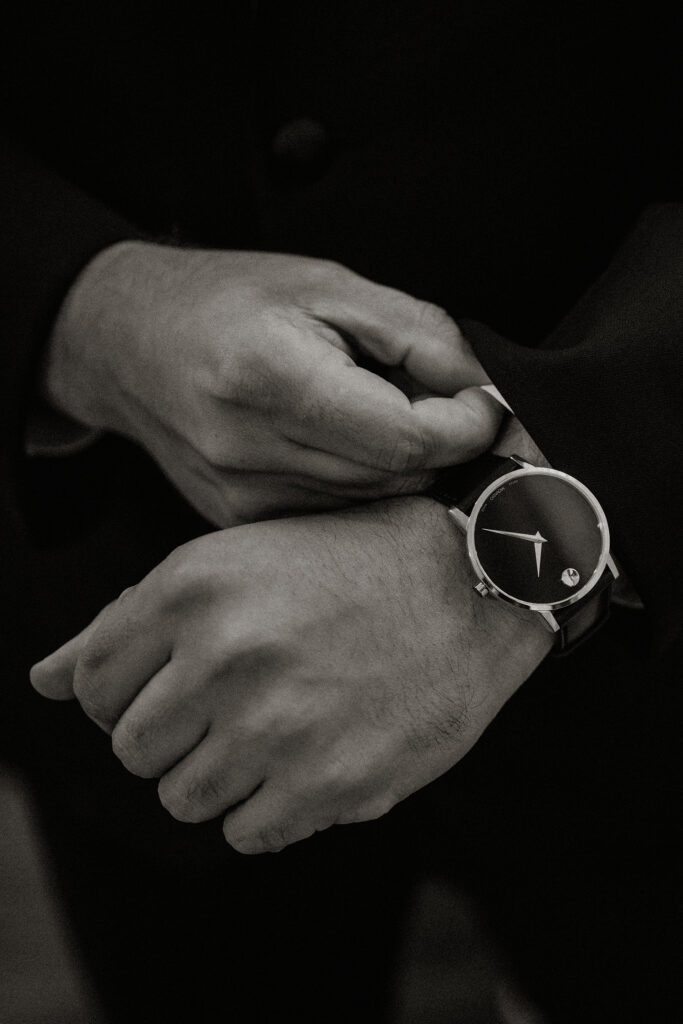 Black and white detail photo of a groom fixing his sleeves and adjusting his special watch.