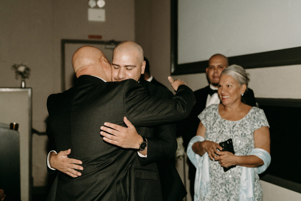 Groom hugging his father after walking into their movie theatre ceremony.