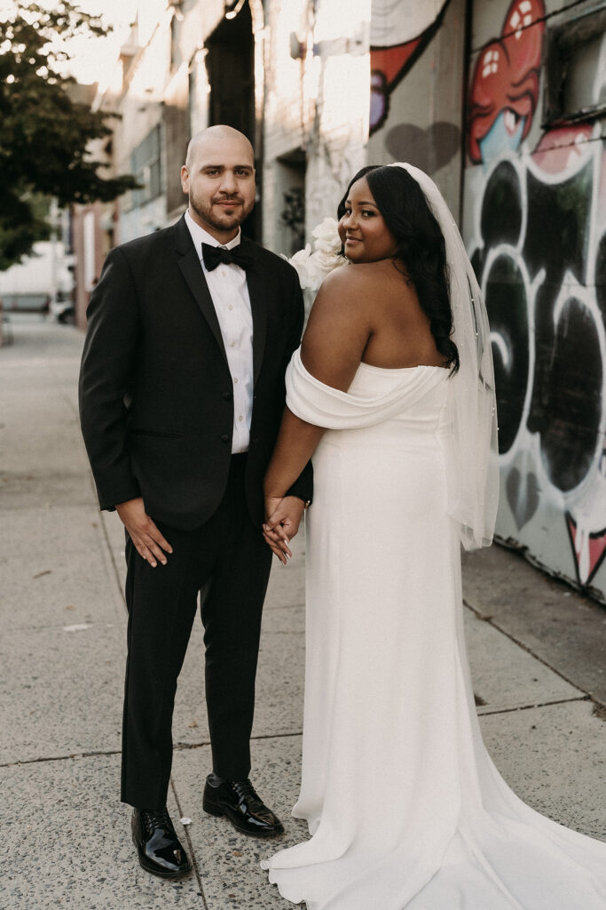 Bride and groom posing during their wedding photos in front of a graffiti wall in Bushwick Brooklyn, NY