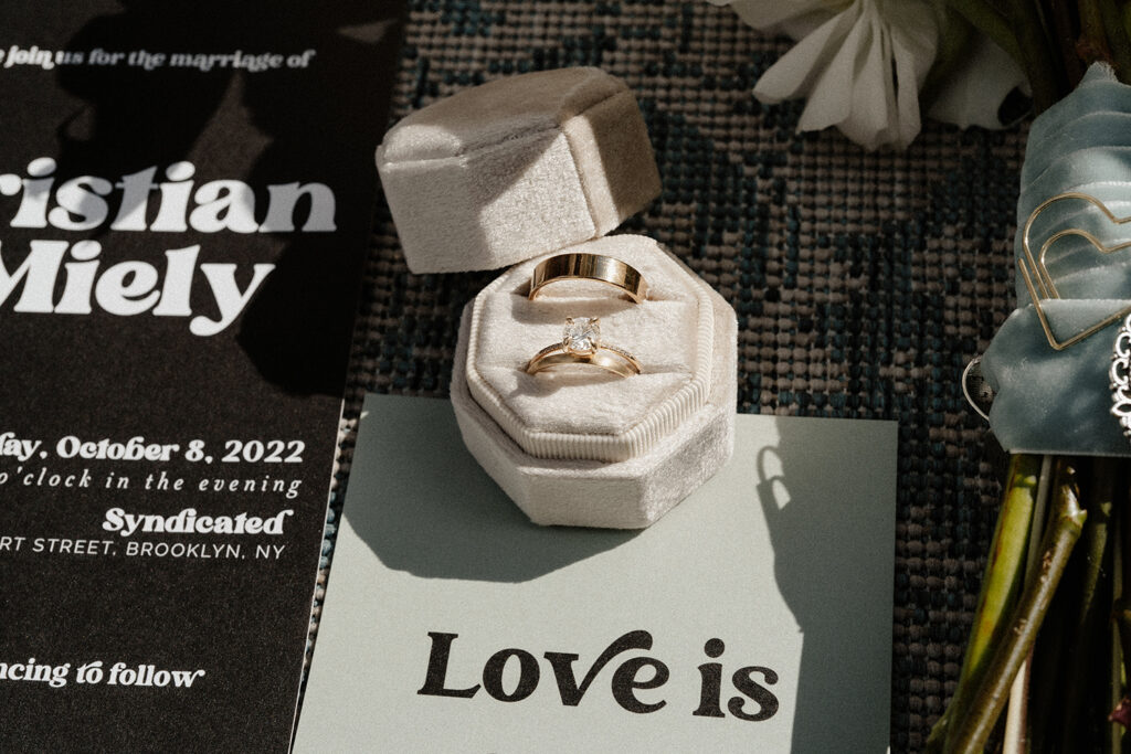 Close up detail photo of wedding rings, ring box, and invitation suite.