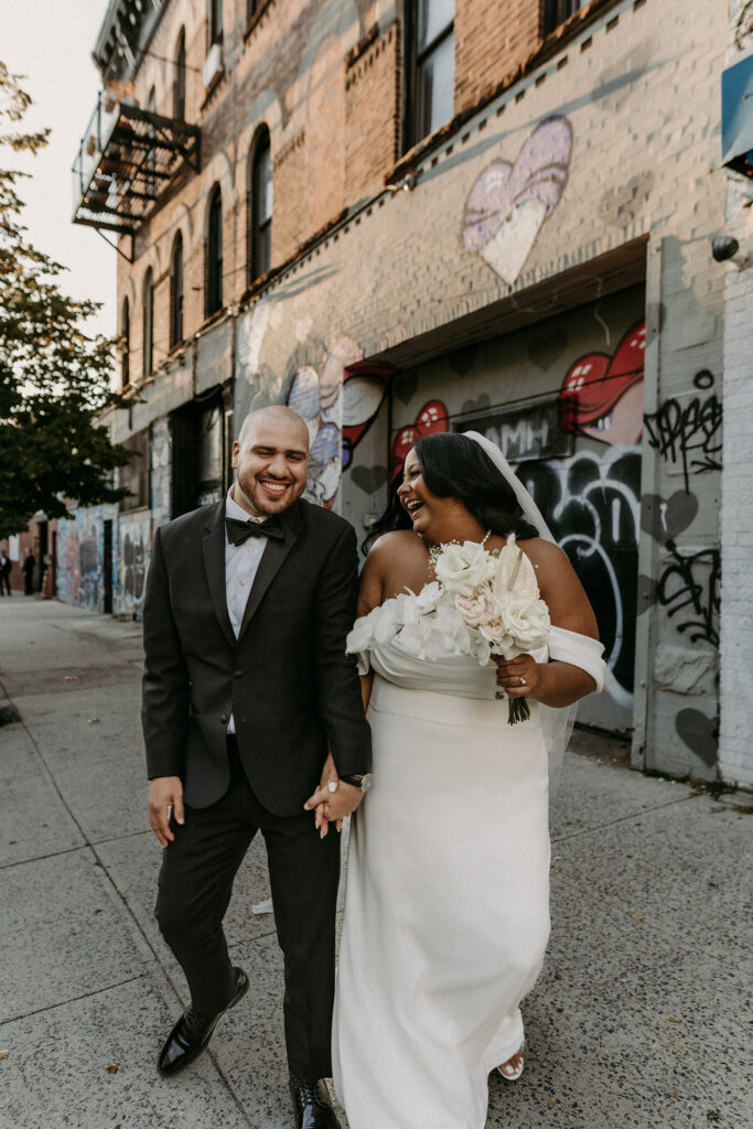 Bride and groom walking together and laughing during their wedding photos in front of a graffiti wall in Bushwick Brooklyn, NY