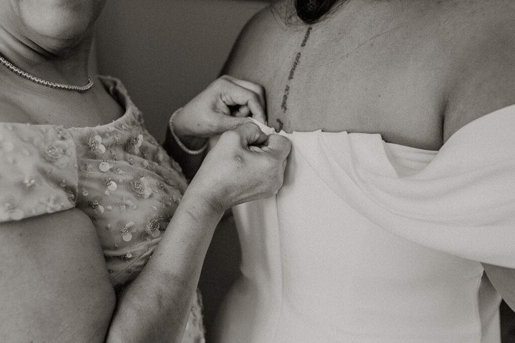 Black and white photo of mother buttoning her daughter's wedding dress.