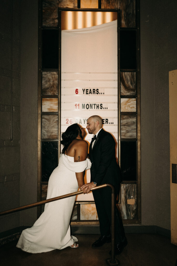 Bride and groom sharing a celebratory kiss in front of their "Now Playing" sign for their movie theatre wedding.