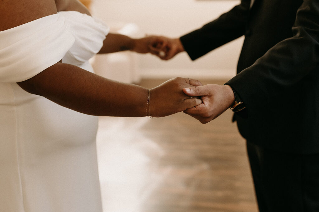 Close up photo of a bride and groom holding hands.