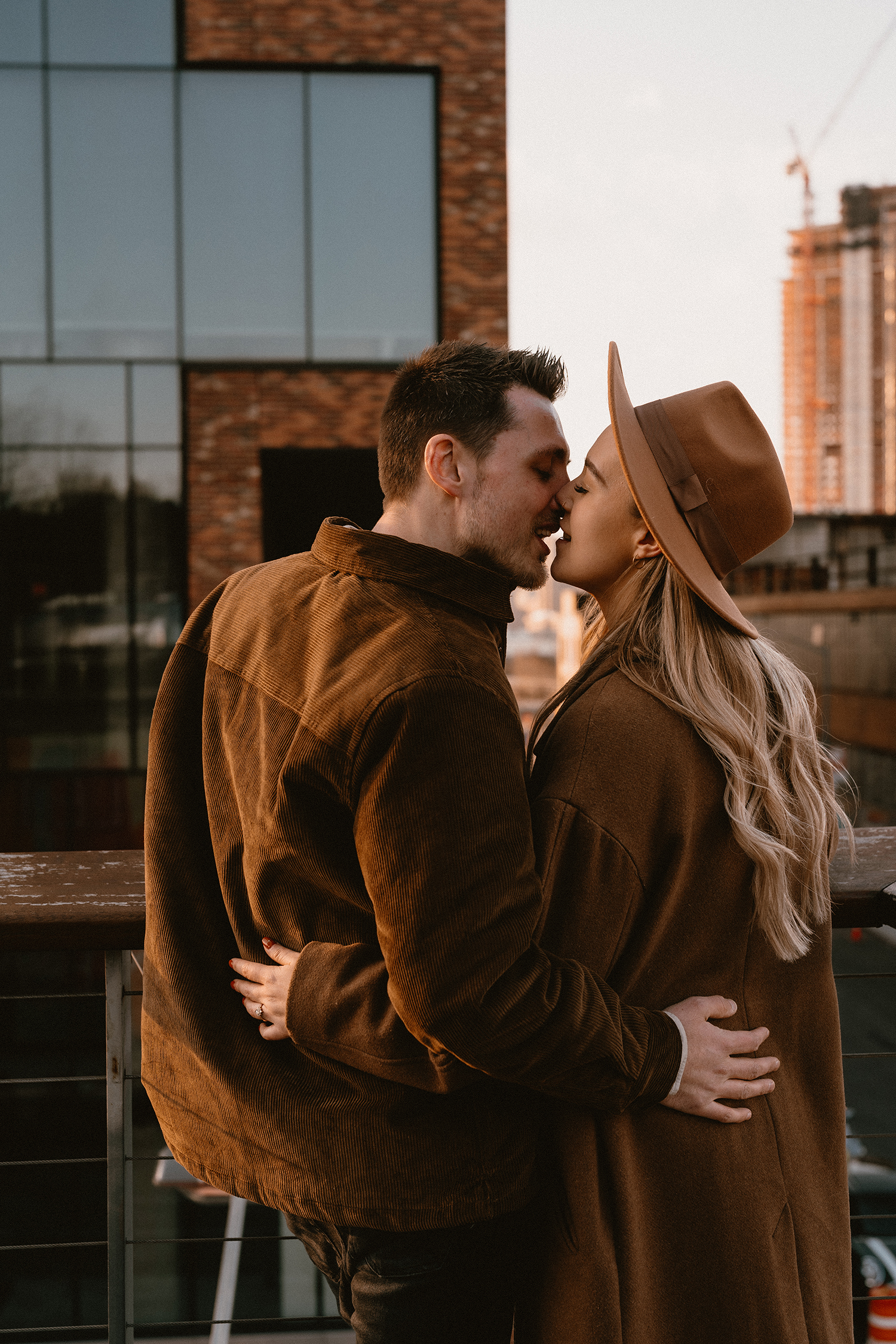 Couple kissing and overlooking the NYC skyline from a rooftop during their engagement photoshoot in