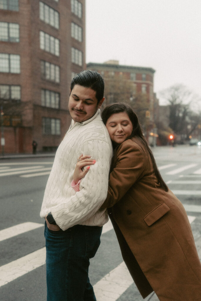 A woman snuggly leans onto her husband on a sidewalk in West Village.