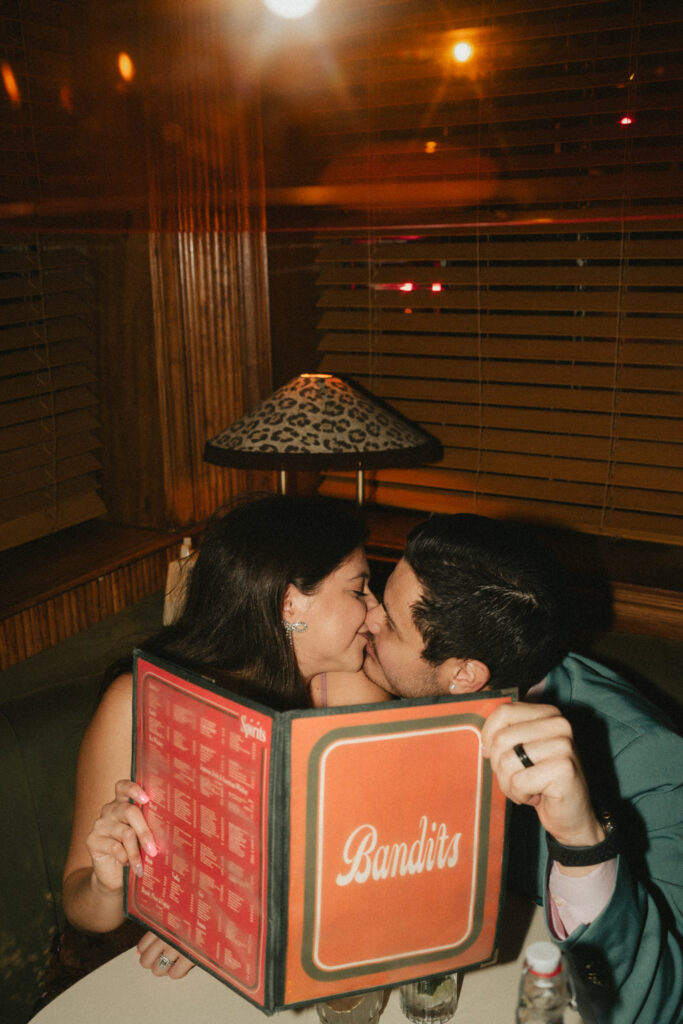 A couple shares a kiss behind the Bandits menu while enjoying this cozy cocktail bar.