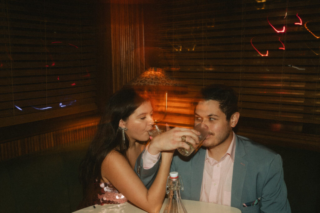 A couple share a moody moment in a warm, retro cocktail bar in west village.