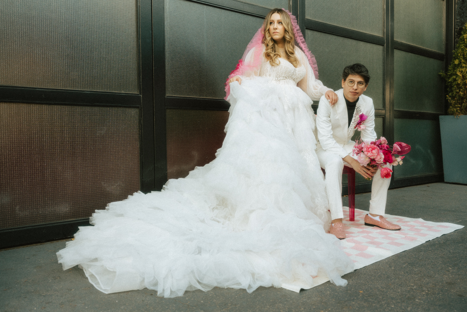 A bride poses with her husband showing off their pink disco wedding details in an editorial wedding portrait.