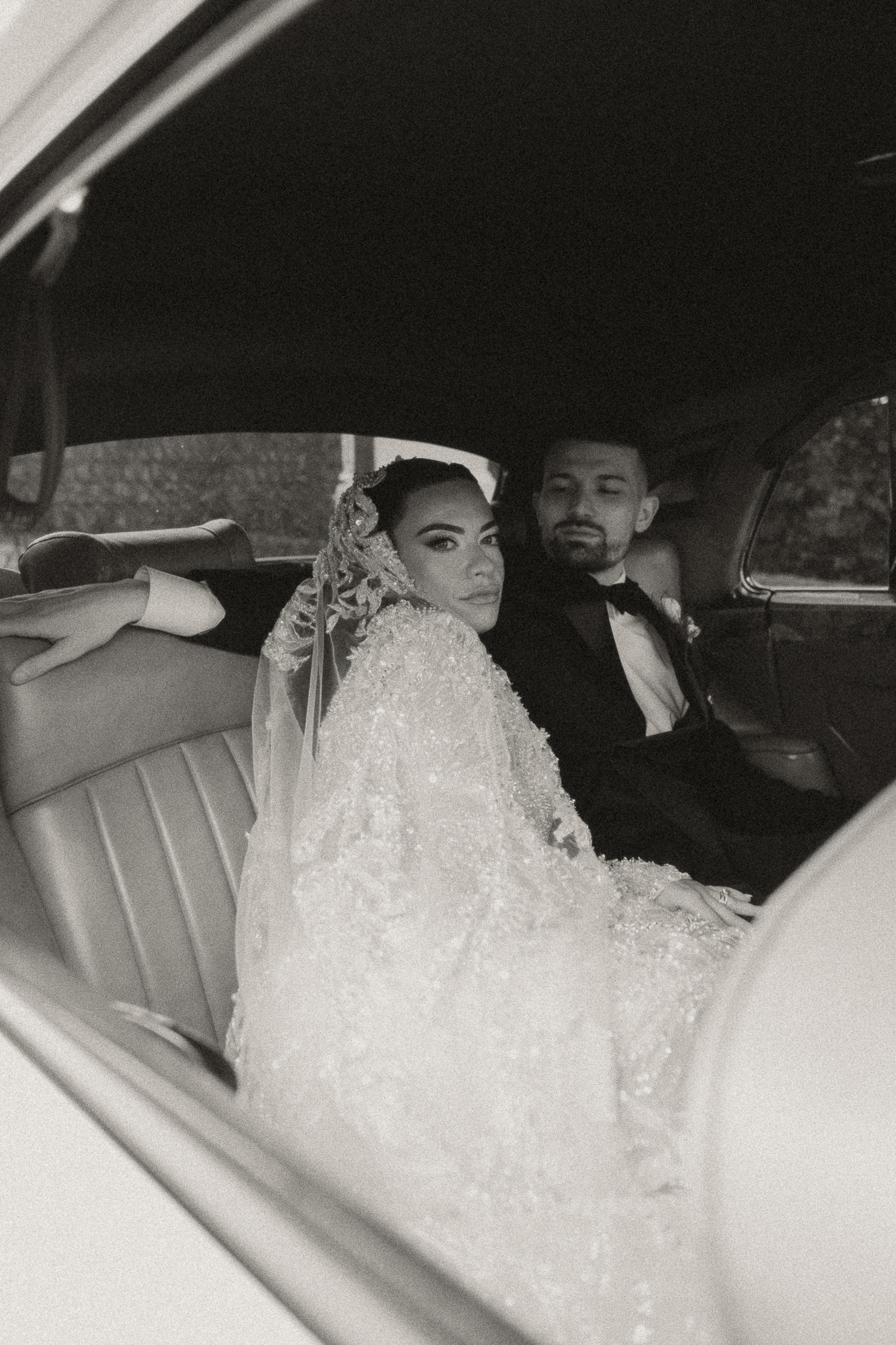 In black and white, Alexa and Anthony sit together in a vintage rolls royce and look out the window.