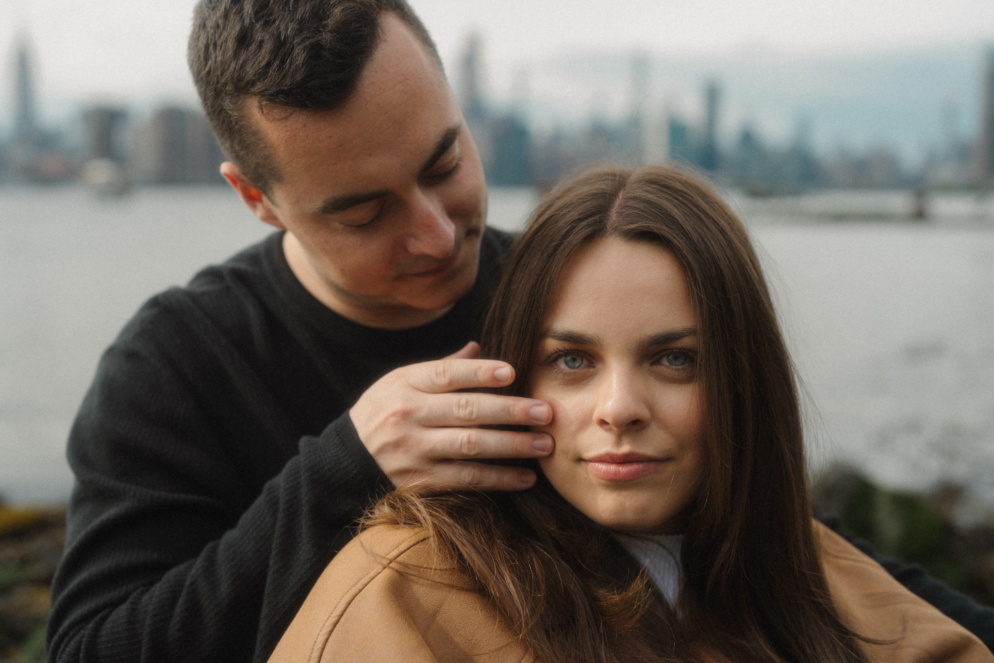 In front of the NYC skyline, Alexis and Vin sit together while he tucks her hair behind her ear.