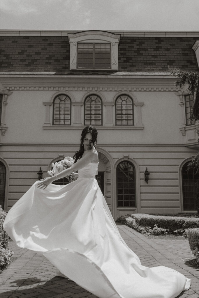 In black and white, a bride twirls her dress around her outside of the Ashford Estate.