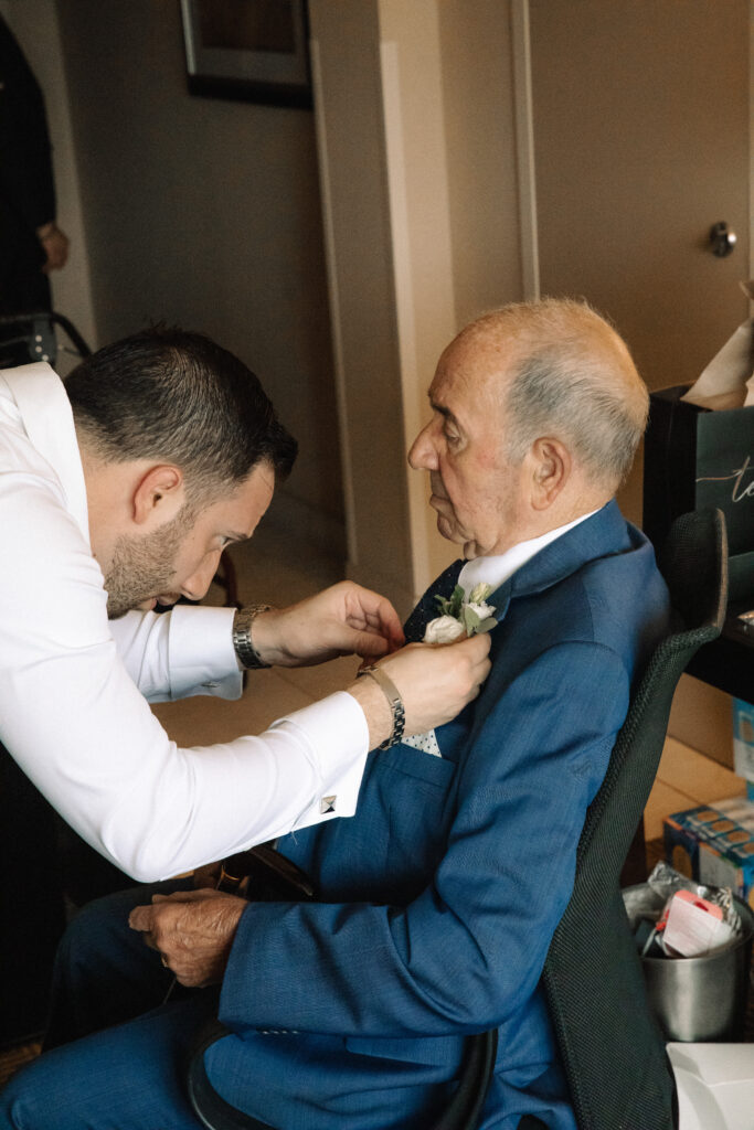 A groom helps his elderly grandfather to put on his boutonnière.