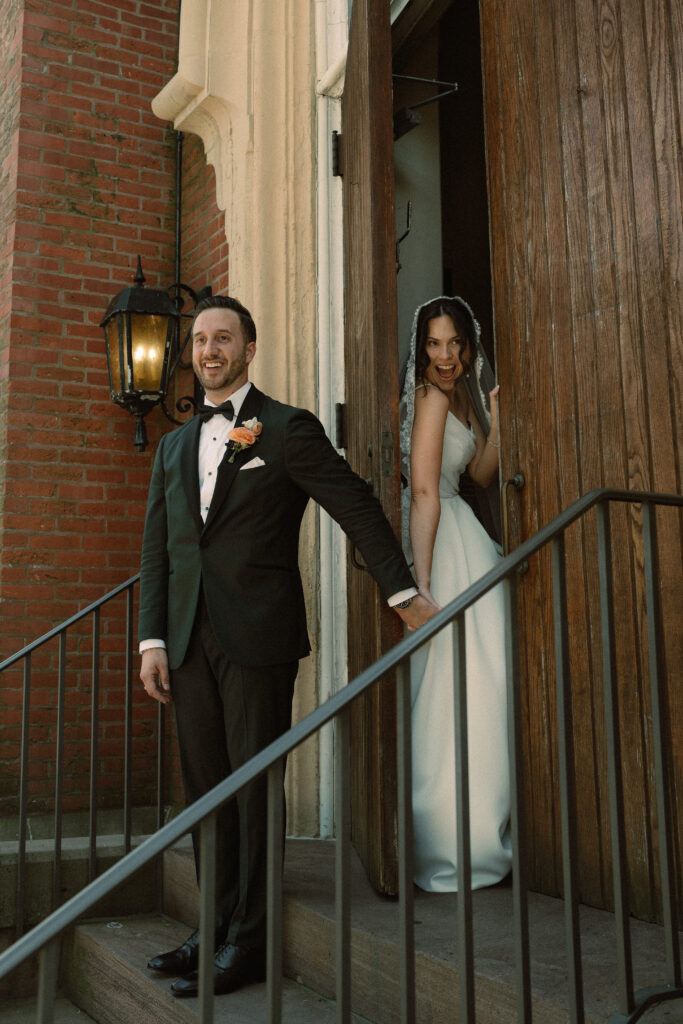 A bride and groom share a first touch with each of them on either side of the cathedral door.