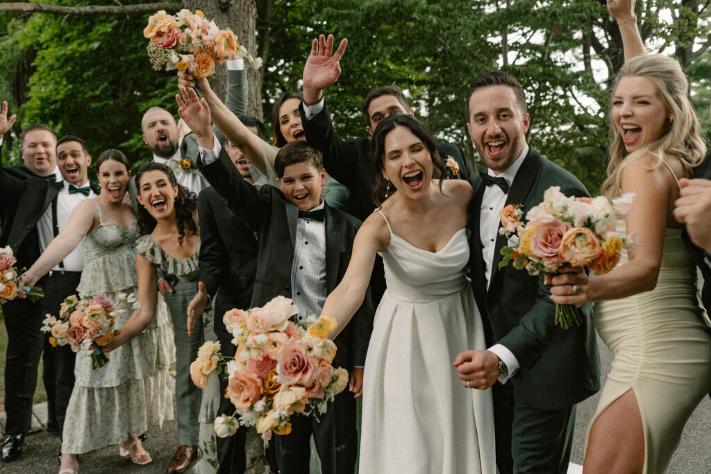 A bride and groom cheer excitedly with their wedding party outside the Ashford Estate.