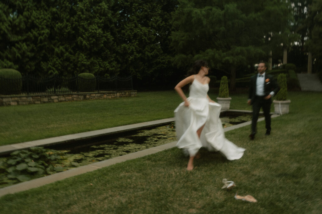 A blurry motion moment of a bride and groom running playfully through the garden at their luxurious venue.