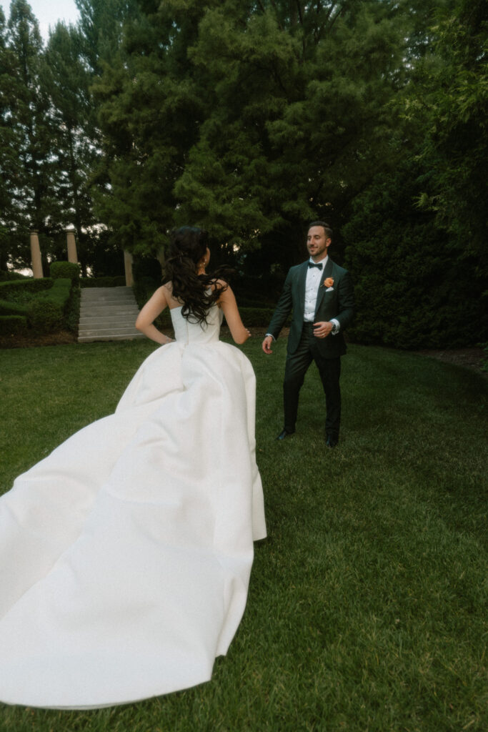 A bride runs towards her groom in a luxurious garden with the long train of her wedding dress flying behind her.