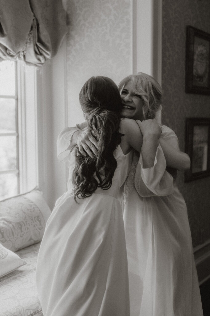 In black and white, a bride and her mom share a tight hug after helping her into the wedding dress.