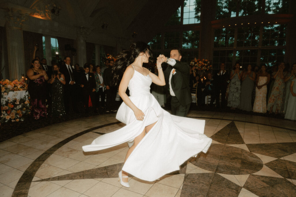 During their first dance, a groom leads his wife into a big spin and her a-line dress flies around her.