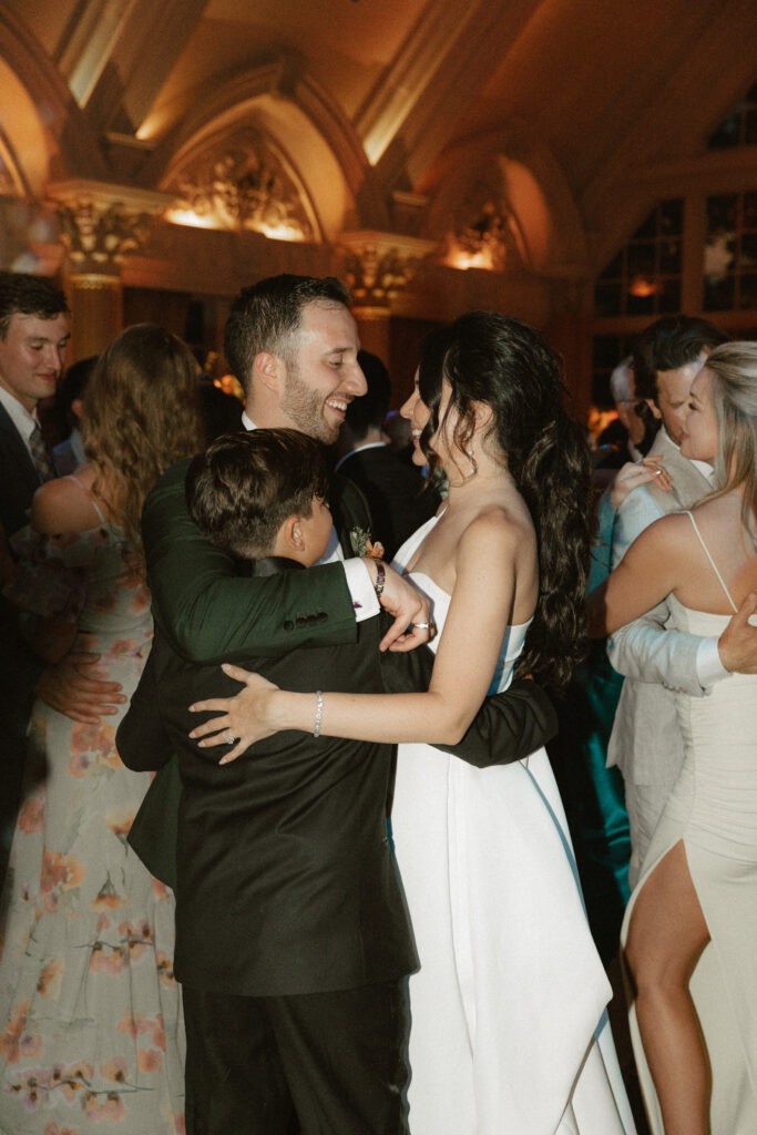 A groom and bride group hug with their son in the middle of the dance floor during their wedding reception.