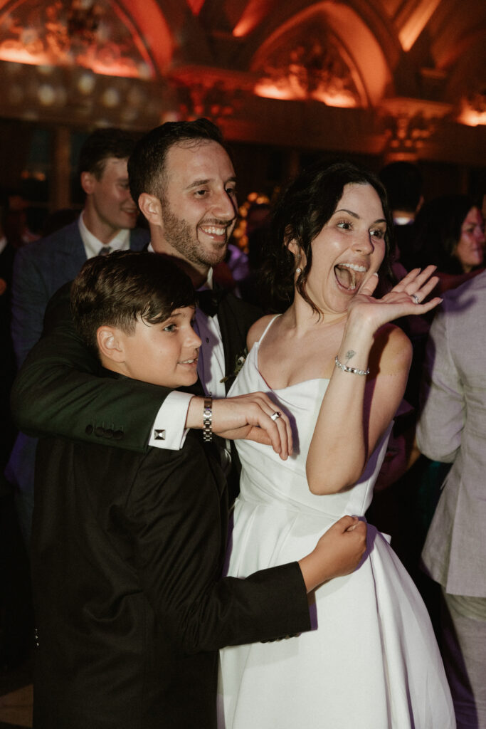 With celebratory smiles, a bride, groom and their son dance together on the dance floor at their wedding reception.