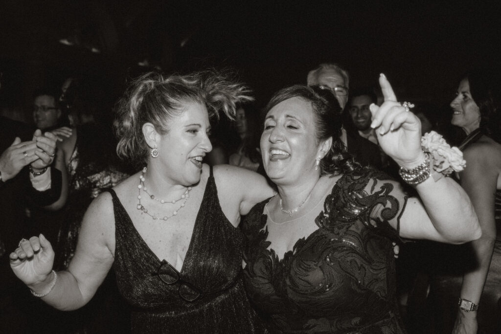 The groom's mom and her friend dancing at the wedding reception, in black and white.