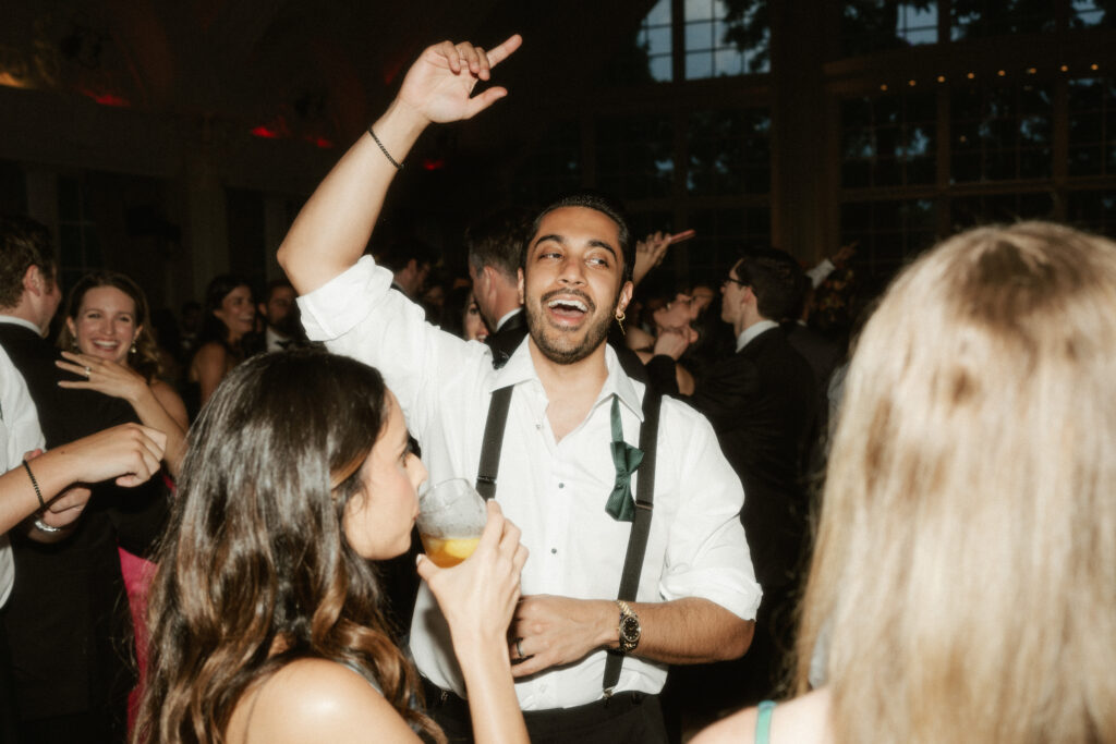 A wedding guest dances with his hands up in the middle of the dance floor.