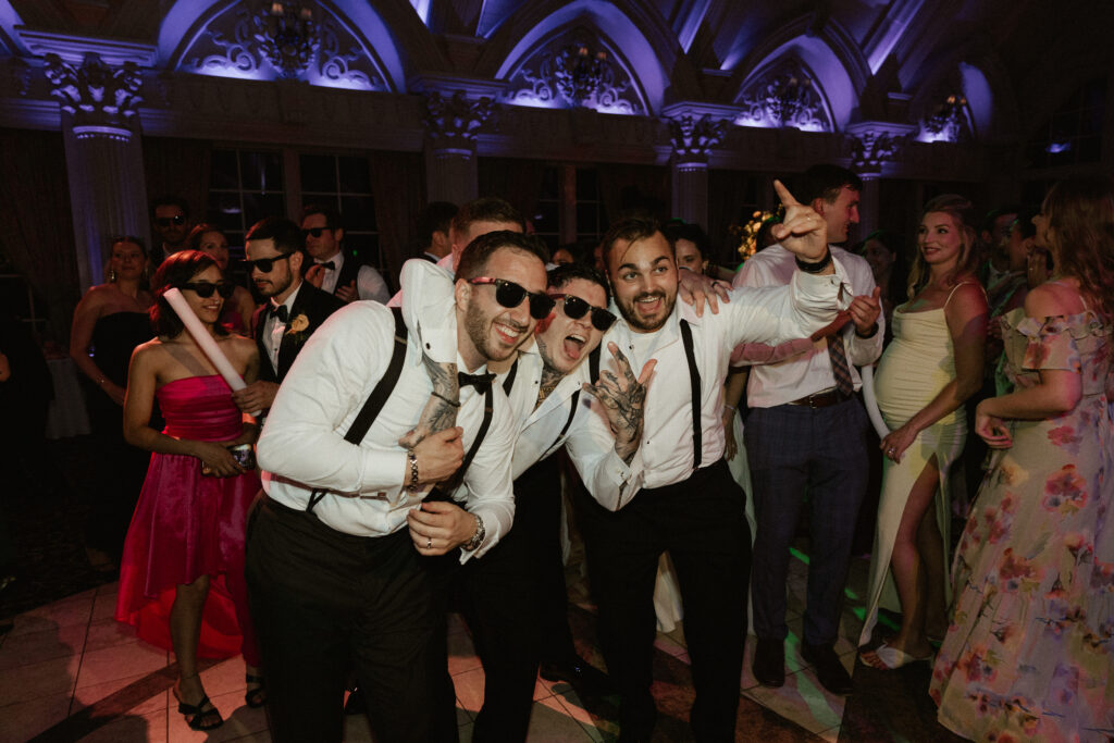 A group of groomsmen dancing arm and arm on the dance floor with the groom.