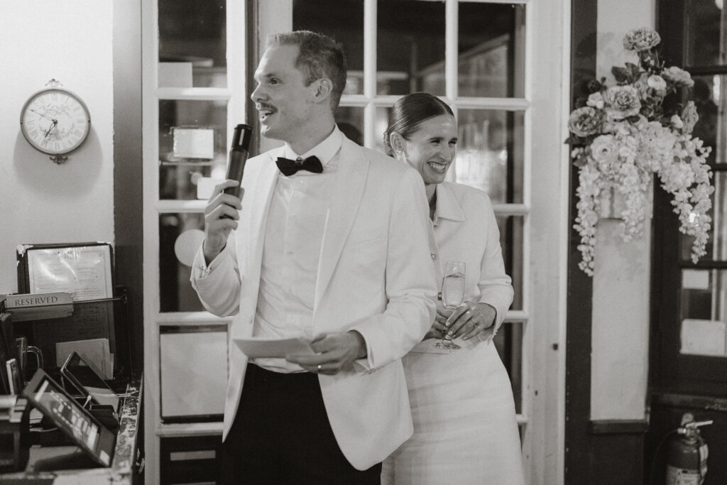 black and white image of bride and groom addressing guests mic in hand