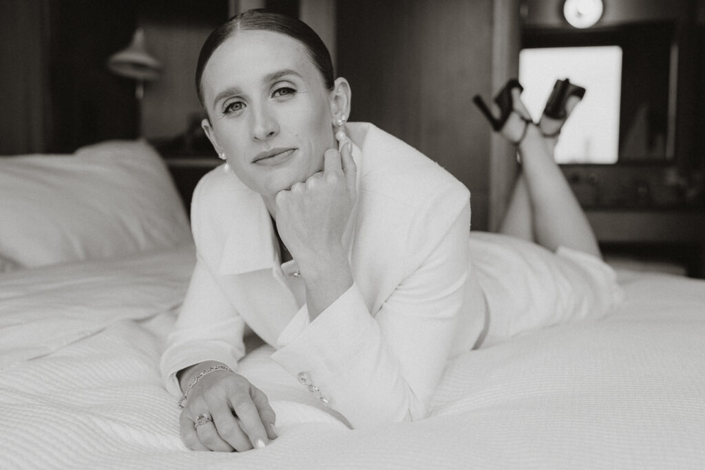 Black White film image of bride lying on stomach dressed for hybrid wedding with hand under chin. 