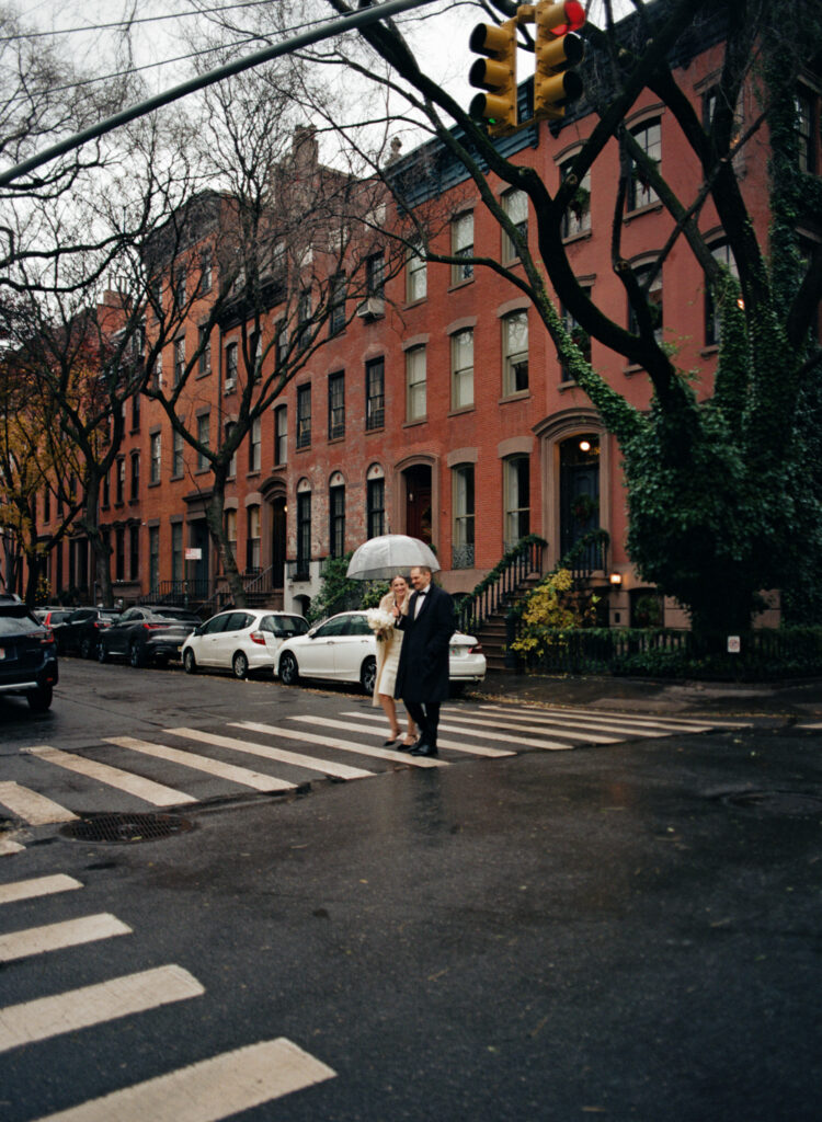 film shot of wedding couple under a clear umbrella walking through NY cross walk