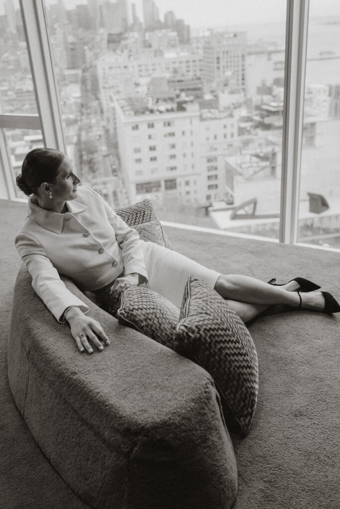 Elongated posed bride looking out window at New York City landscape