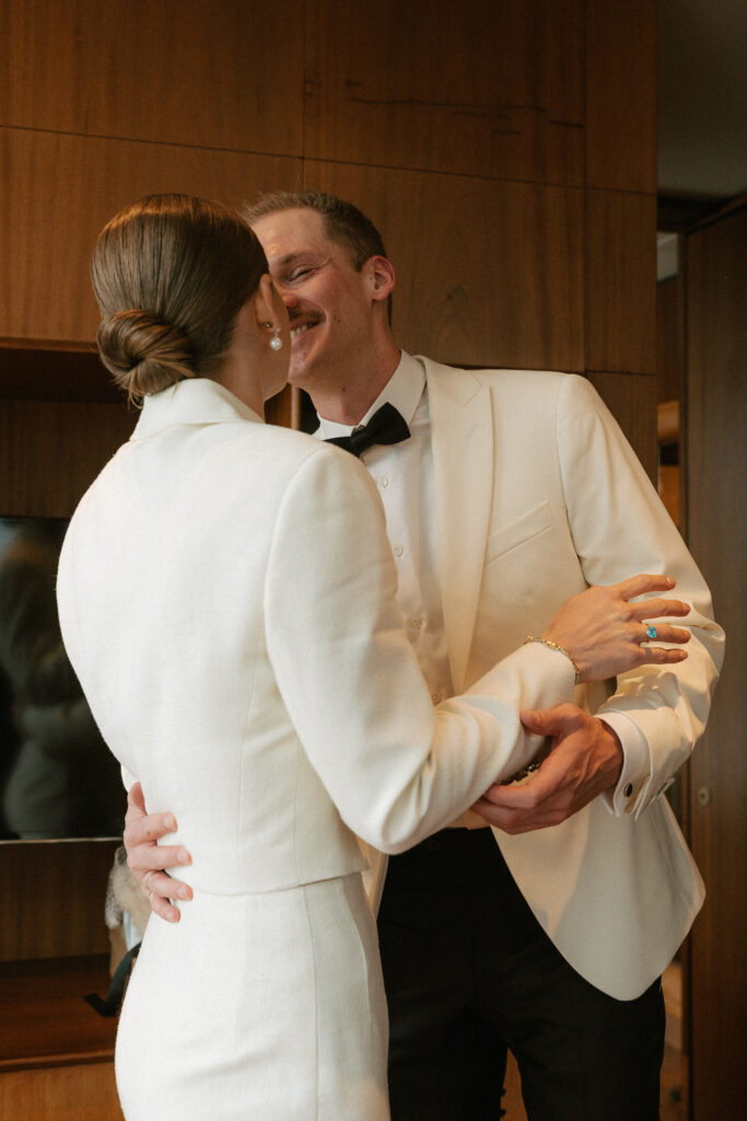 Groom going in for kiss with a cream colored blazer white shirt black bow tie and pants