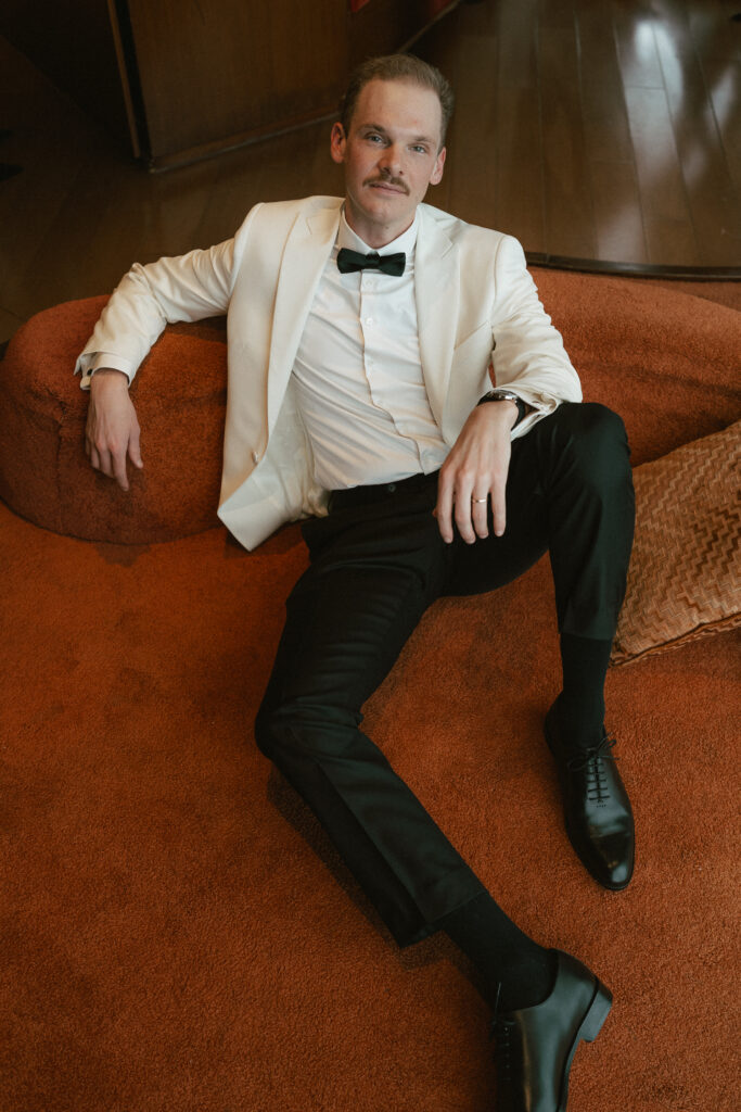 Groom dressed for wedding lounging on vintage carpet in penthouse of the Standard Hotel 