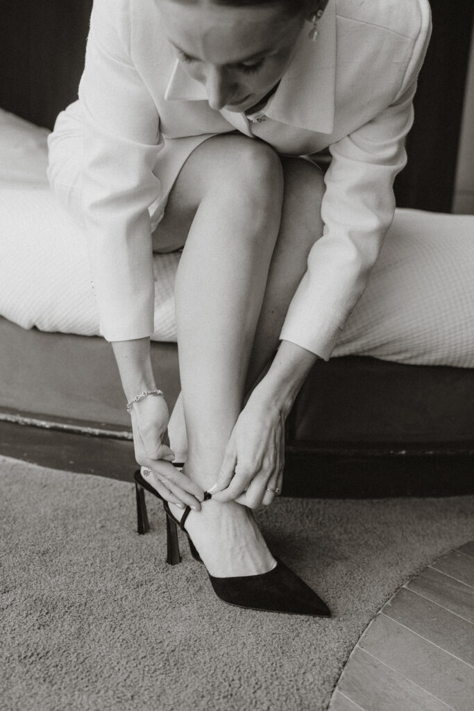 Bride's hands in frame strapping on elegant classy Christian Louboutin black heels. 
