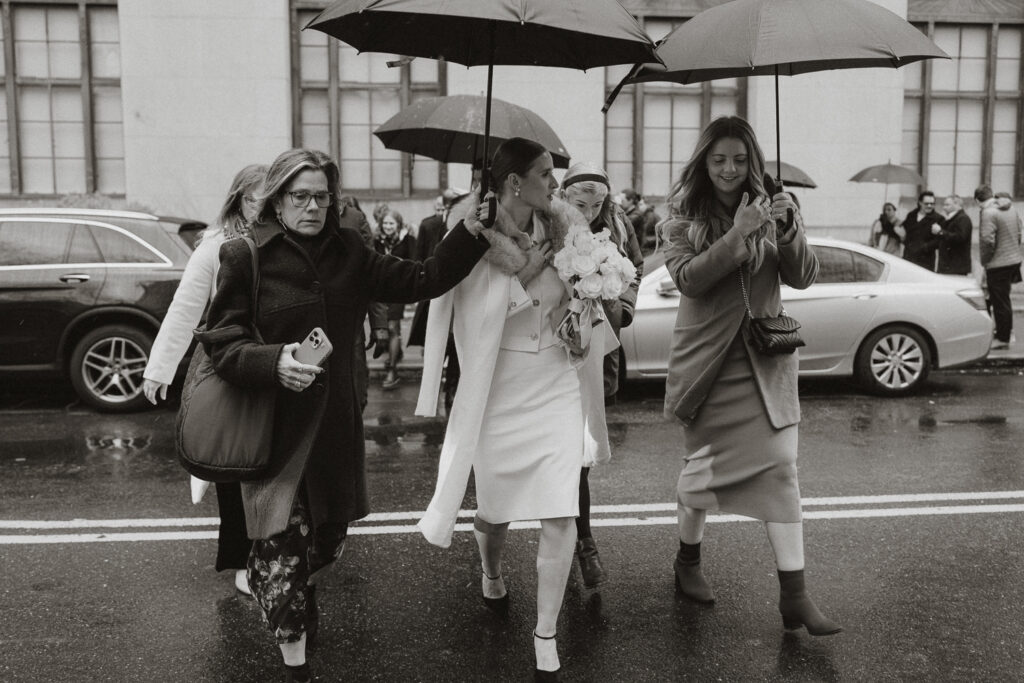 umbrellas up to cover bride as she crosses a Manhattan street 