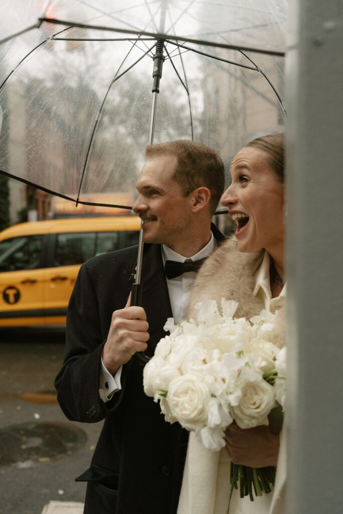 Candid shot of newly married couple under clear umbrella and NY taxi in background