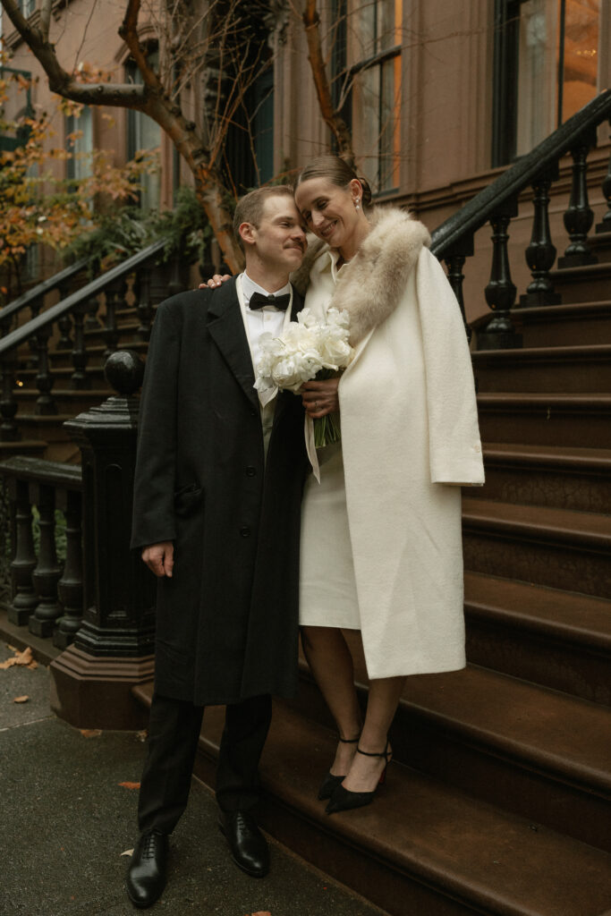 Brownstone steps offer an elegant backdrop for wedding couple dressed in winter fashion on a cloudy day