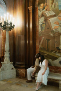 Engaged couple lean in for a romantic photo with the NY Library Art display as background