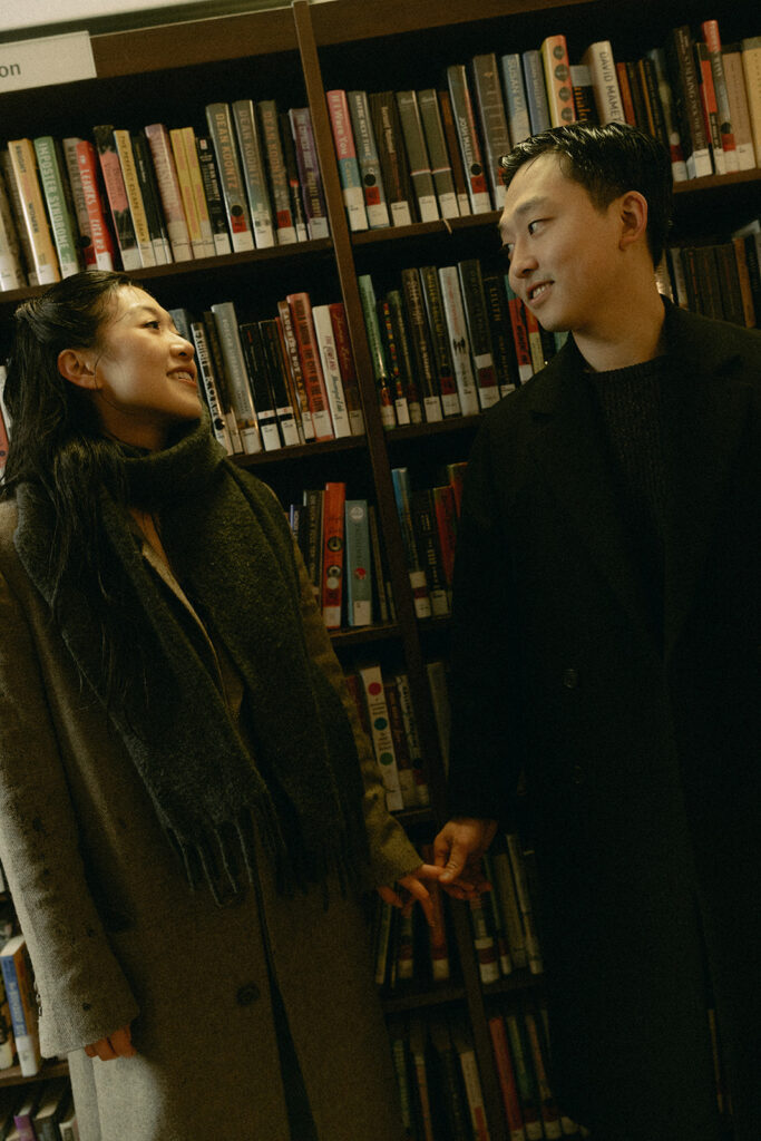 Warm and cozy engagement photos in a library for a winter photoshoot.